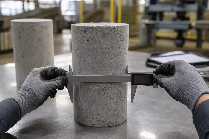 A technician measuring a cast concrete test cylinder with digital calipers during quality control